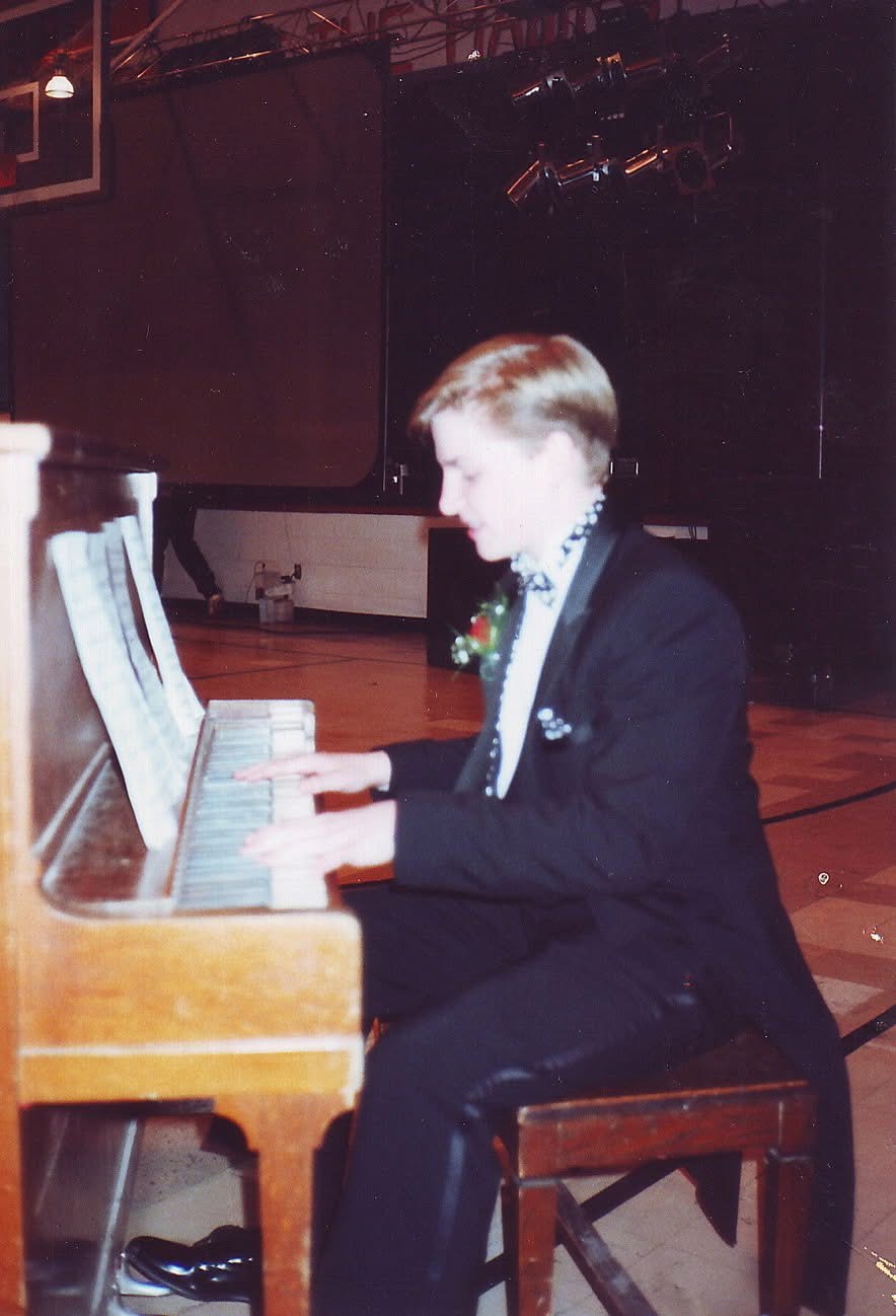 Matthew Mayer as a young pianist in a tuxedo performing on an upright piano at a school gymnasium event